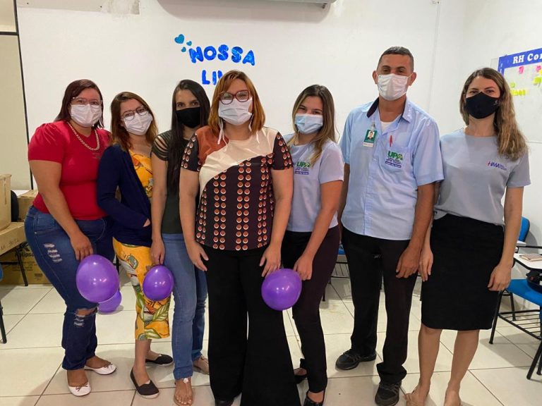 Colaboradores participantes do treinamento. Eles estão lado a lado e de frente para a câmera. Todos usam máscara e alguns seguram um balão roxo na mão.